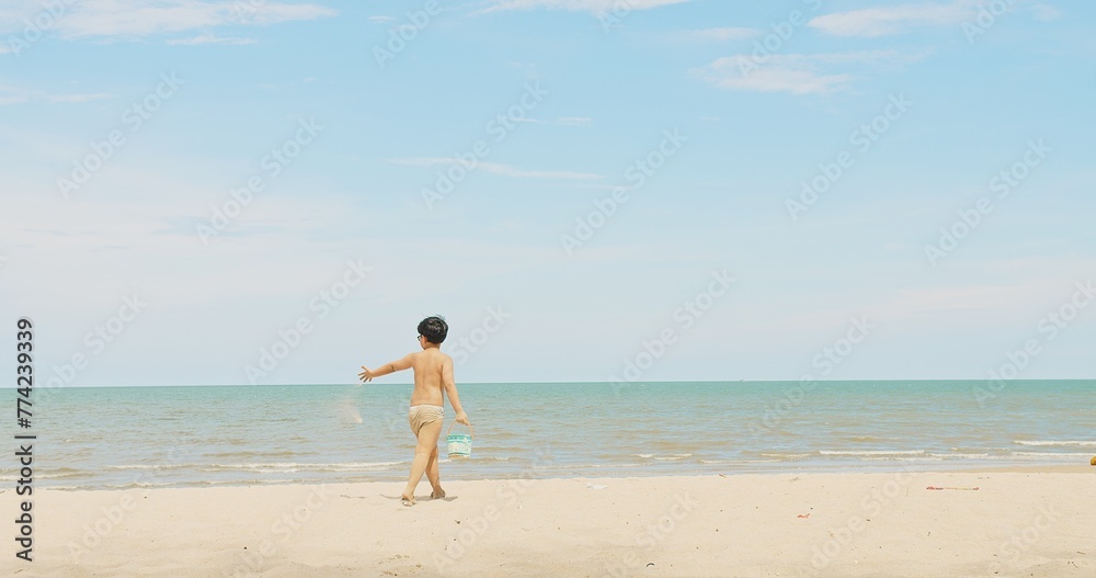 active happy cute Asian children boy enjoy leisure summer vacation holiday travel walking on tropical ocean sea beach and playing sand on sunny day blue sky background