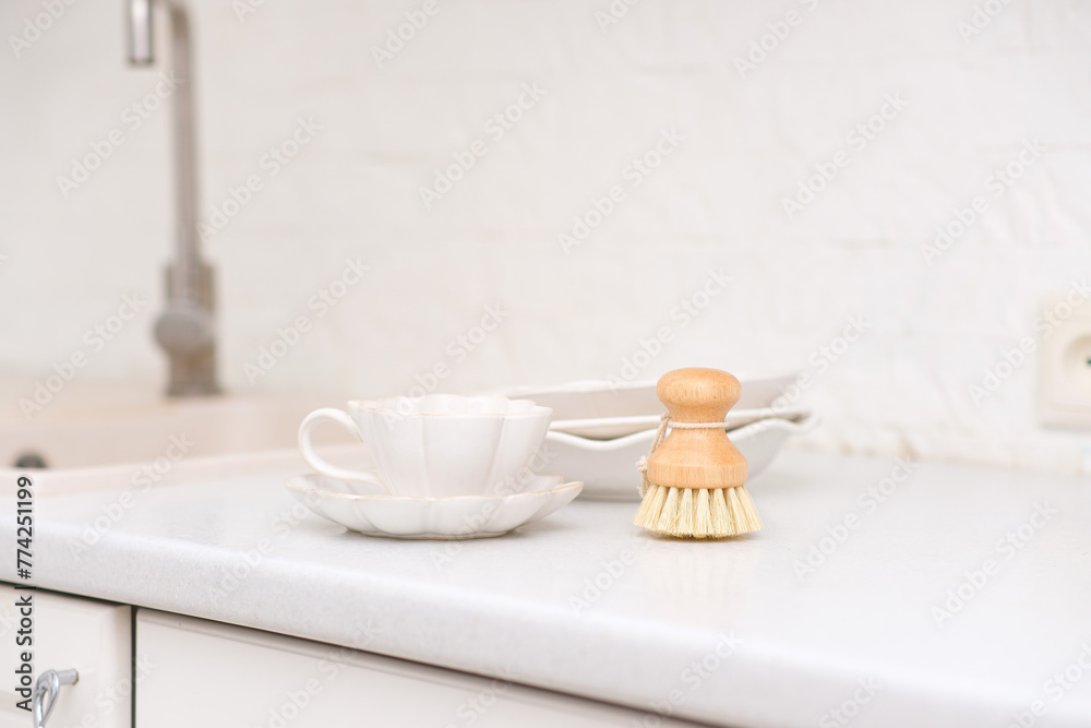Side view of bamboo dishwashing brushes near sink and plates on table in kitchen. Washing dishes. Home comfort. Eco-friendly kitchenware. Household equipment. Concept of cleanliness
