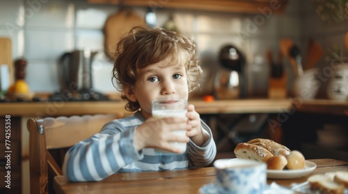 Child with curly hair drinking milk for breakfast. Casual morning routine scene in a home setting. Healthy eating habits concept.
