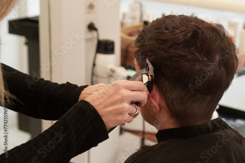 An hairdresser cutting a costumer sideburns with an electric razor