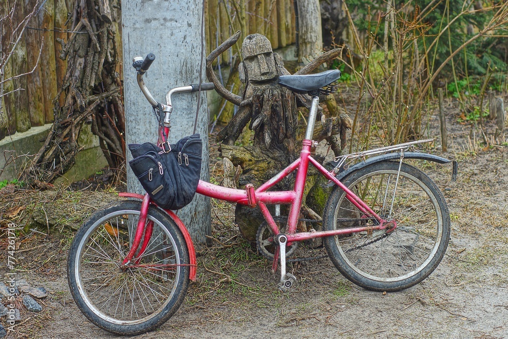 an old small iron retro red bicycle without a frame with a black bag on the handlebar stands on the ground near a concrete gray pillar during the day on the street an old small iron retro red bicycle without a frame with a black bag on the handlebar stands on the ground near a concrete gray pillar during the day on the street