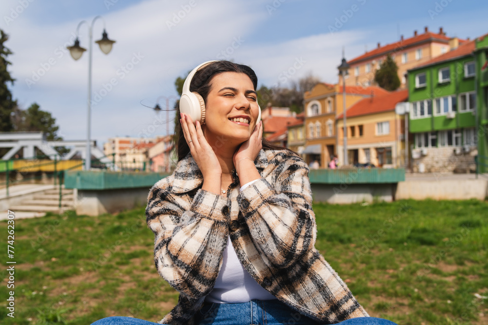 One young girl or woman is listening to music on her wireless headphones and enjoying the sun outdoors	
