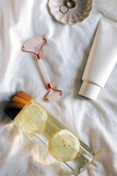 Morning routine accessories on the bed, water with lemon, face roller and lotion