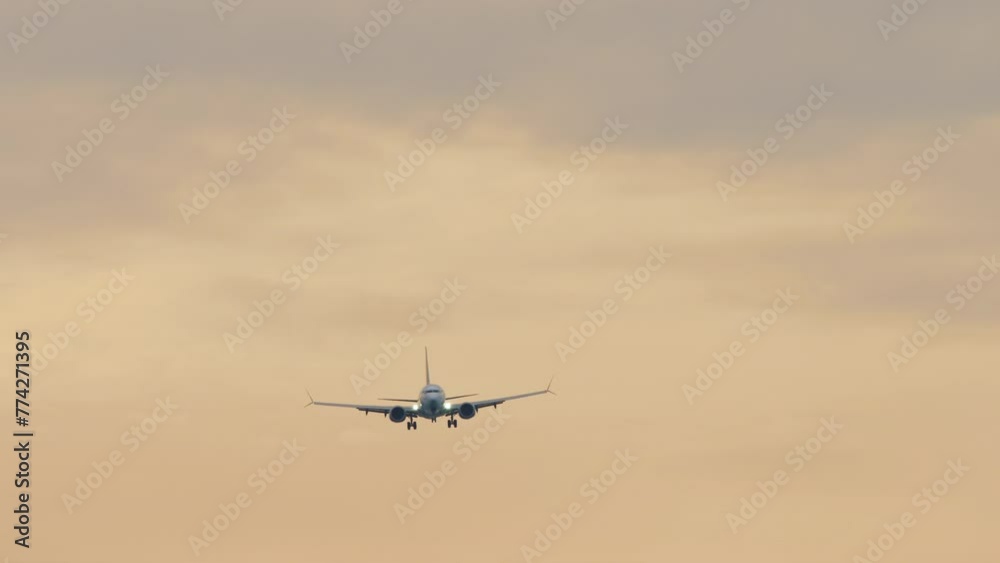 Long shot of an airplane silhouette in a golden sunset sky. Airliner approaching for landing, front view Long shot of an airplane silhouette in a golden sunset sky. Airliner approaching for landing, front view