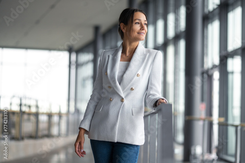 Confident elegant woman in white jacket standing in the premises with big windows