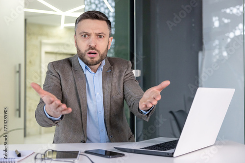 Canvas Print Portrait of a befuddled businessman in an office setting looking directly at the camera with a confused expression and hands up in a questioning manner