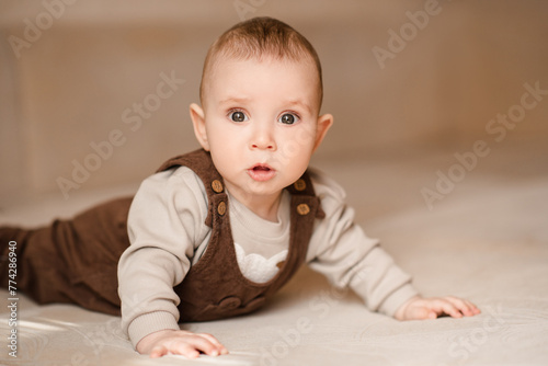 Upset baby boy crawling in bed looking at camera close up. Childhood. © morrowlight