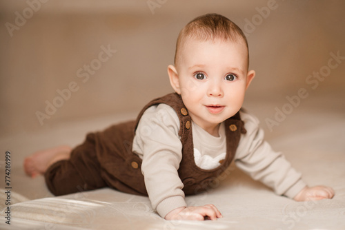 Smiling baby boy 4-5 months old crawling in bed looking at camera close up. Child wearing cute stylish clothes. Childhood. © morrowlight