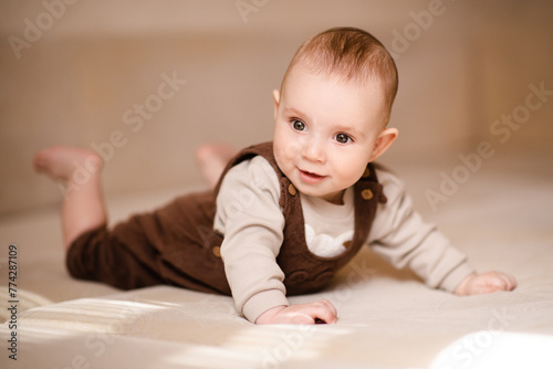 Smiling baby boy 4-5 months old crawling in bed close up. Child wearing cute stylish clothes. Childhood. © morrowlight