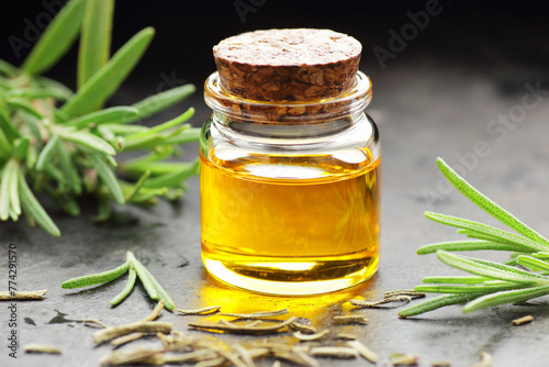 Rosemary essential oil on black texture background with fresh leaves nearby, copy space, natural medicine, organic remedy for hair, skin care, stress therapy