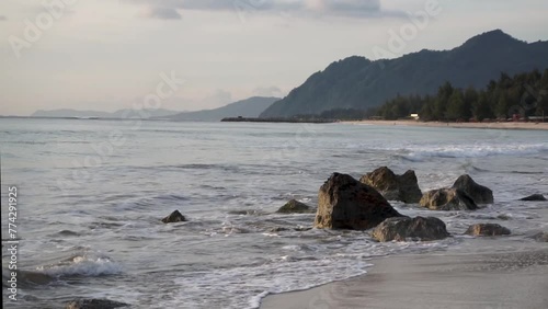 Wave smashing giant causeway stone in Lampuuk Beach Banda Aceh, Indonesia. Popular tourist destination in Aceh. Beach landscape with mountain view background at the sunset. photo