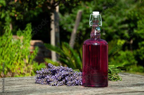 Home made lavender syrup on old wooden table with a bouquet of lavender flowers. Home made lavender syrup in buckled bottle on old, rustic wooden table outdoor in bright sunshine in summer.