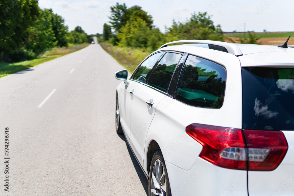 A white car is parked on a sunny road, ready for a journey amidst greenery and clear skies. The scene exudes tranquility and adventure.