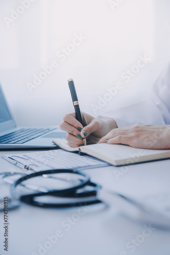 Doctor and patient sitting at the desk in clinic office. The focus is on female physician's hands filling up the medication history record form, close up. Medicine concept
