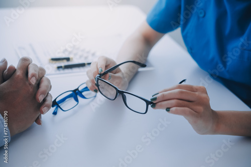 Close-up of Asian female doctor talking with elderly patient showing eyeball model and explaining eye disease in hospital
