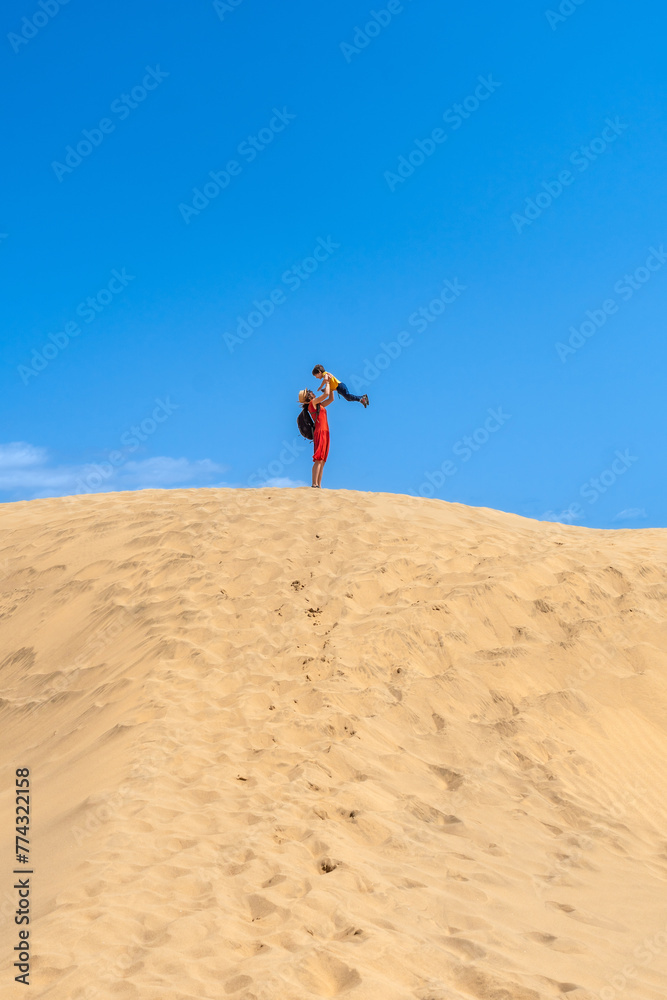Mother lifting child smiling in the dunes of Maspalomas on vacation, Gran Canaria, Canary Islands Mother lifting child smiling in the dunes of Maspalomas on vacation, Gran Canaria, Canary Islands