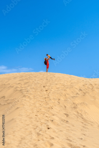 Mother lifting child smiling in the dunes of Maspalomas on vacation, Gran Canaria, Canary Islands