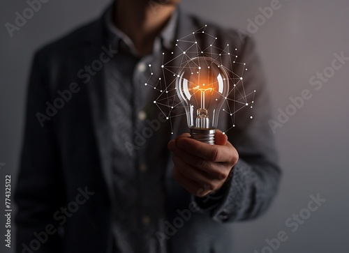 Businessman holding a light bulb with a digital network connection on a grey background 