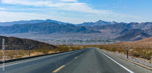 Straight asphalt road in a rocky desert in a valley towards high mountains, California