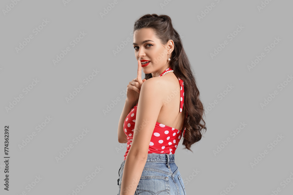 Portrait of beautiful pin-up woman showing silence gesture on grey background Portrait of beautiful pin-up woman showing silence gesture on grey background