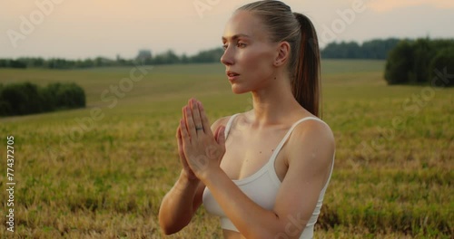 Young woman doing yoga in nature, wearing a white top and olive-colored shorts.