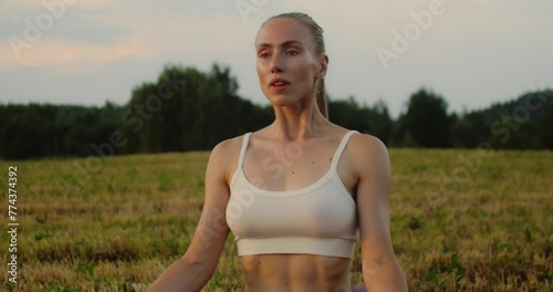 Young woman doing yoga in nature, wearing a white top and olive-colored shorts.