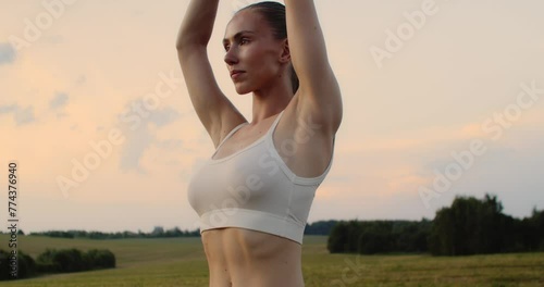 Young woman doing yoga in nature, wearing a white top and olive-colored shorts.
