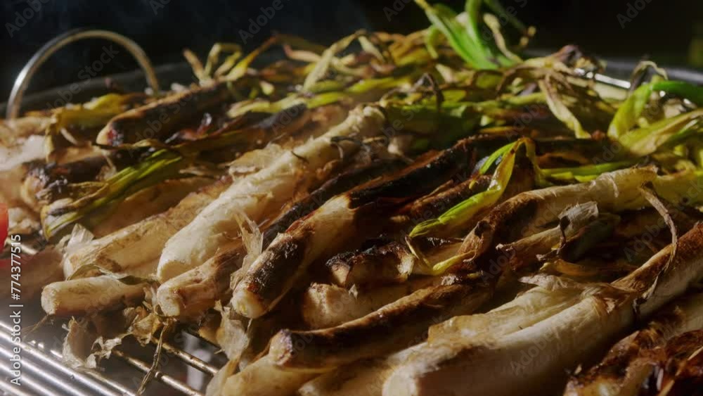 Traditional Spanish catalan green winter onion calcots, spring green season grill barbecue, vegan bbq with fire in Barcelona, Catalonia. Close up of grilling green onion.