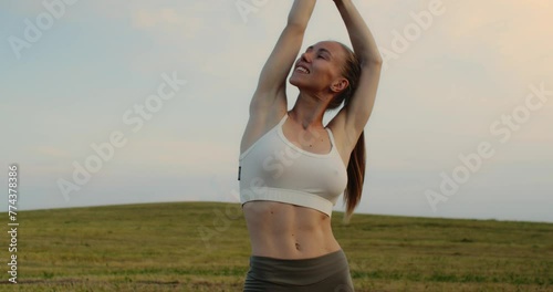 Young woman doing yoga in nature, wearing a white top and olive-colored shorts.