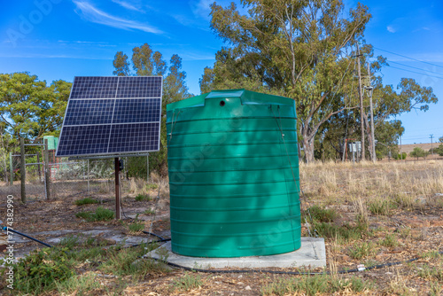 Close up on Solar panels and a large green plastic water tank.  Concept for Solar power to pump underground water for consumption. 