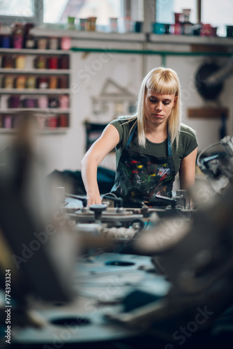 Focused female graphic worker preparing screen printing press for work