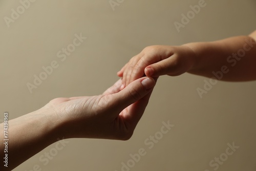 Mother and child holding hands on beige background, closeup