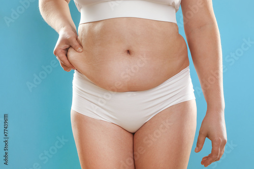 Woman touching belly fat on light blue background, closeup. Overweight problem © New Africa