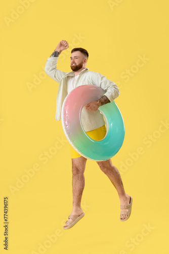 Young man with inflatable ring jumping on yellow background