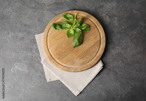 Fototapeta Naklejka Na Ścianę i Meble -  Wooden cutting board, fresh basil and napkin on grey table, top view