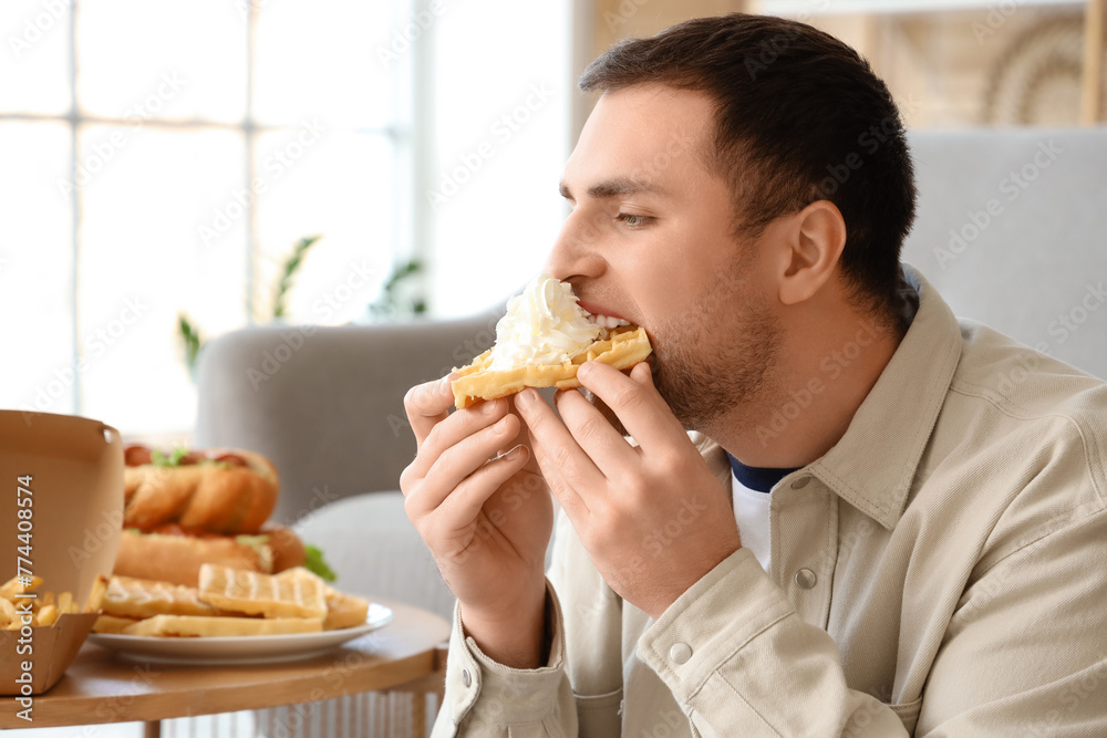 Young man eating waffle at home, closeup. Overeating concept Young man eating waffle at home, closeup. Overeating concept