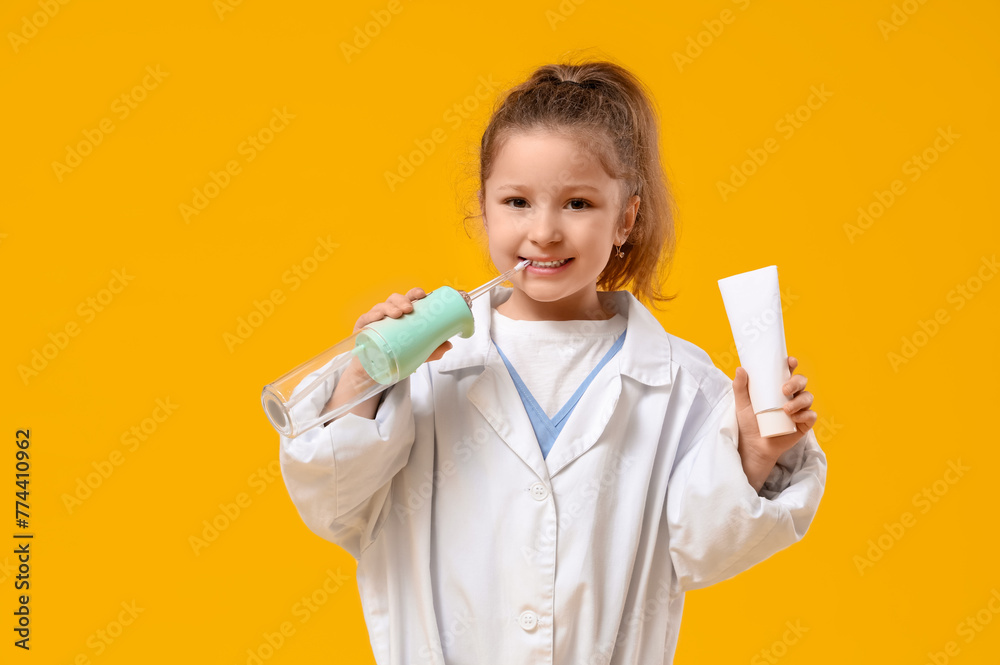 Cute little dentist with oral irrigator and tube of paste on yellow background Cute little dentist with oral irrigator and tube of paste on yellow background