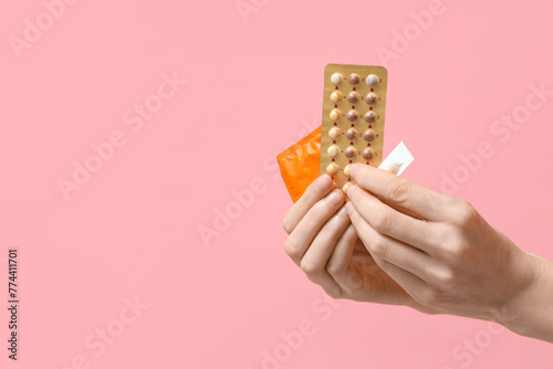 Female hands with birth control pills, vaginal suppositories and condom on pink background photo