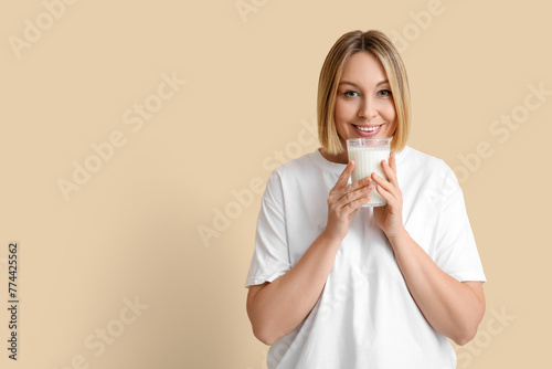 Beautiful young woman with glass of fresh milk on beige background