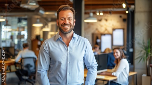 A smiling CEO standing in a bright  open-concept workspace with colleagues working in the background
