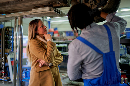 In the workshop, a woman client and a mechanic with tools, discussing car troubles. A scene of communication and guidance.
