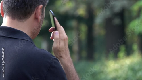 Unrecognizable man filmed from behind dialing a phone number on a smartphone and then making a phone call