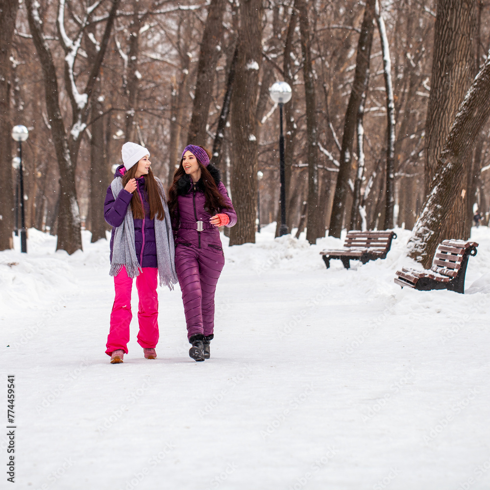 Two young happy girlfriends walking in a winter park