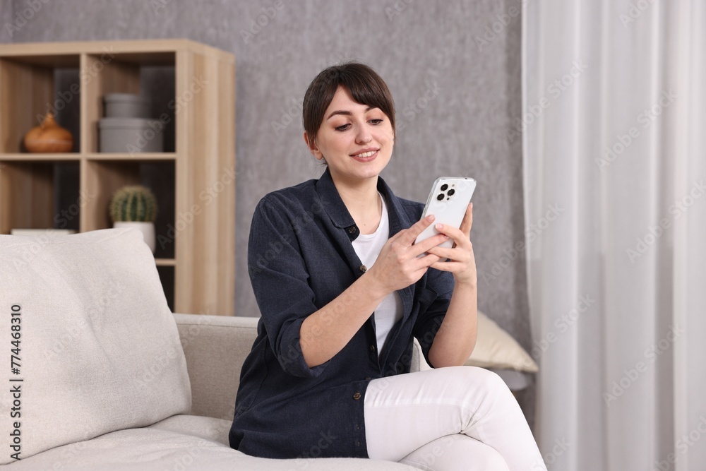 Beautiful young housewife using smartphone on sofa at home Beautiful young housewife using smartphone on sofa at home