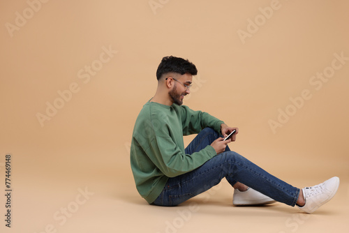 Handsome young man using smartphone on beige background, space for text © New Africa