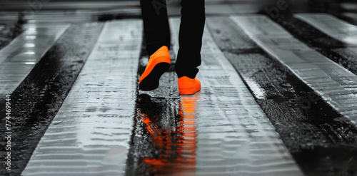 Schritte im Regen: Eine Person in schwarzer Hose und leuchtend orangefarbenen Schuhen geht auf nassem Untergrund über einen Zebrastreifen. 