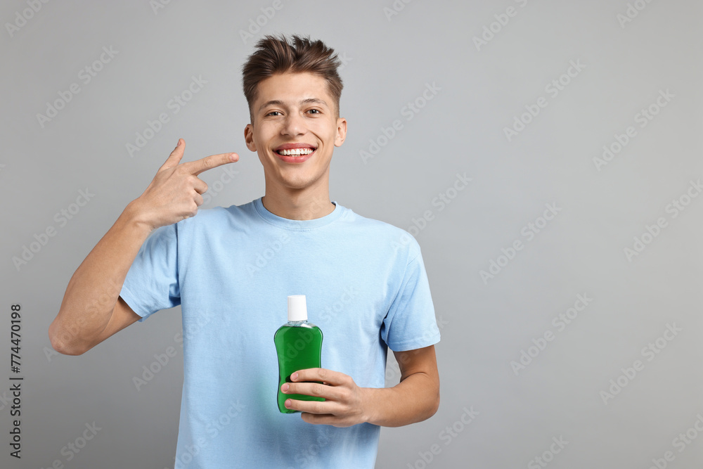 Young man with mouthwash pointing at his healthy teeth on light grey background, space for text Young man with mouthwash pointing at his healthy teeth on light grey background, space for text