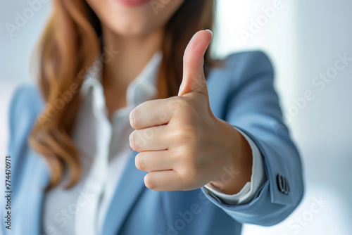 Businesswoman in a blue jacket is giving a thumbs up. Lady Manager with approval gesture in a professional corporate setting.