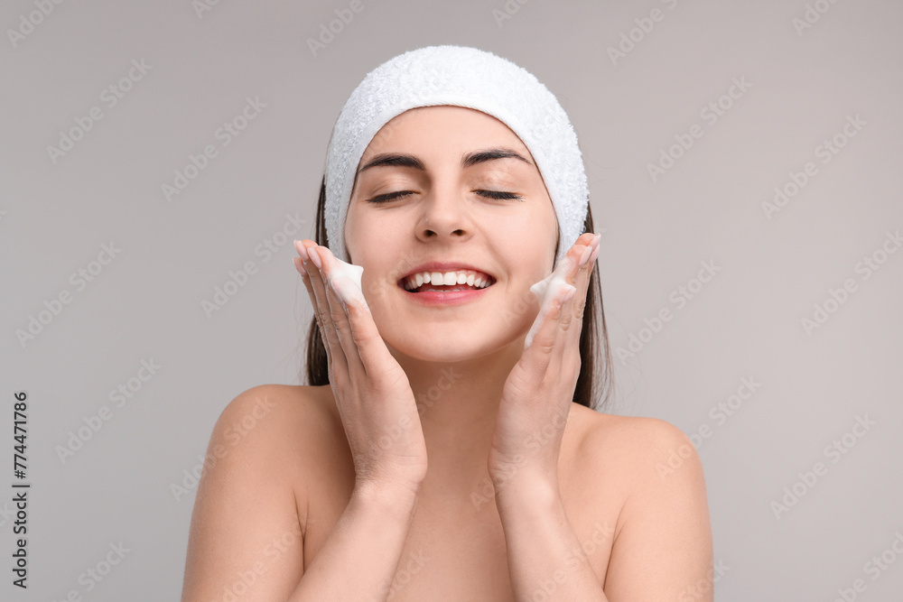 Young woman with headband washing her face on light grey background Young woman with headband washing her face on light grey background