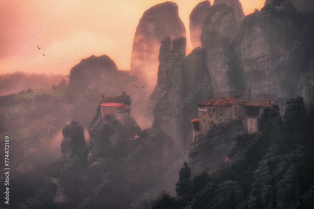 Beautiful misty moment in the rocks of Meteora in Greece at sunset surrounded with monasteries and flying birds. 
